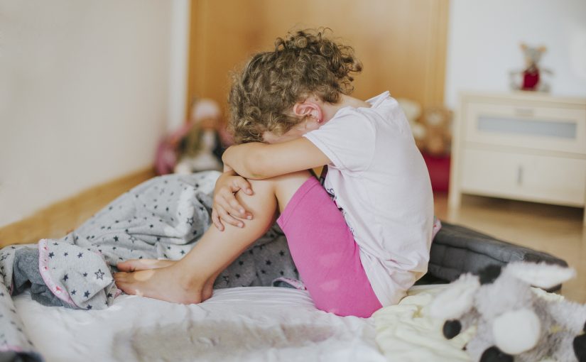 Bettnässen - ein trauriges Mädchen sitzt auf dem nassen Bett