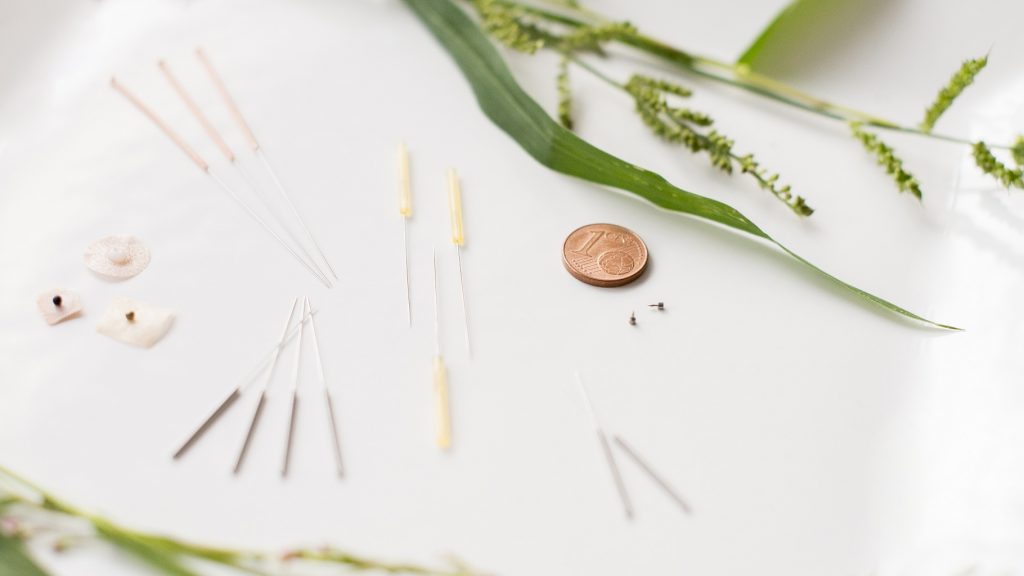 Unterschiedliche Akupunkturnadel und Akupunkturkügelchen sind am Tisch ausgelegt. Sie sehen winzig im Vergleich zu 5-Cent Münze aus.