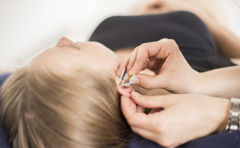 Eine Frau liegt und entspannt sich. Sie bekommt eine NADA Therapie - die fünfte Nadel wird in das Ohr gesetzt.